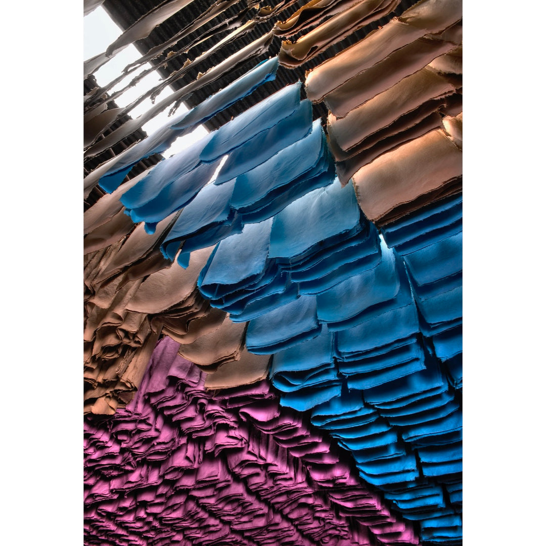 rows of hang drying colored paper high in air sectioned by color like blue orange and pink