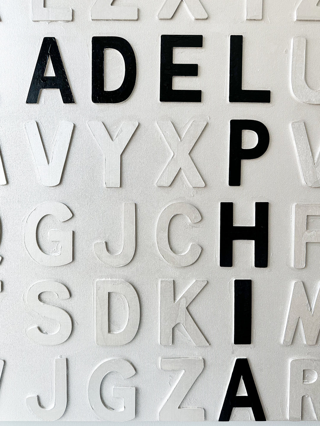 Steffanie Gerkin’s Bad Things White 3D is a contemporary mixed-media typography artwork made with raised wood and acrylic letters on canvas, featuring a white alphabet grid with bold black letters that spell “Bad Things Happen in Philadelphia.”
