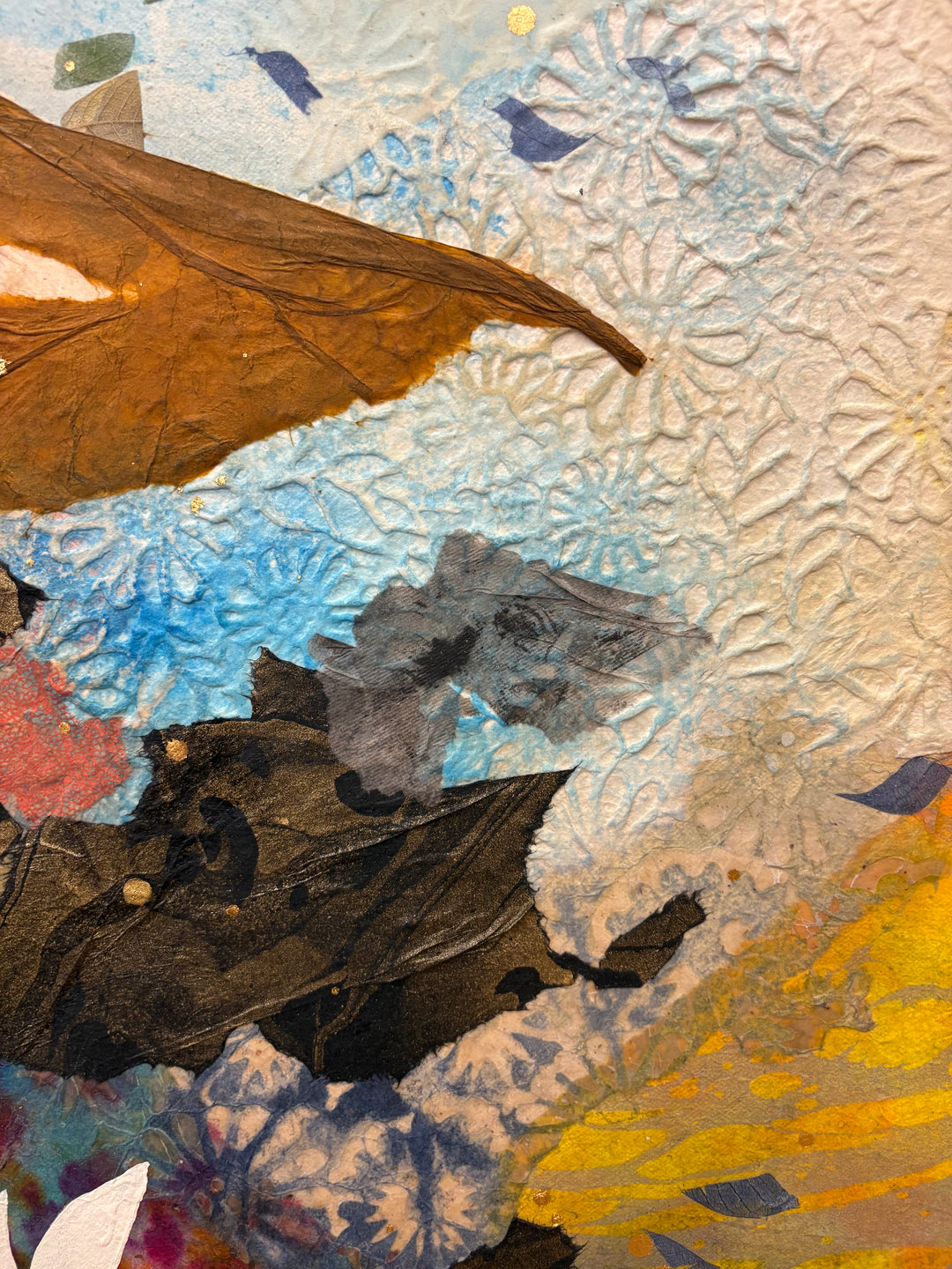 Detail shot of Born to Bloom by Christopher Peter — close-up of textured mixed media surface with a pressed autumn leaf, embossed floral paper, and blue and gold acrylic paint layers