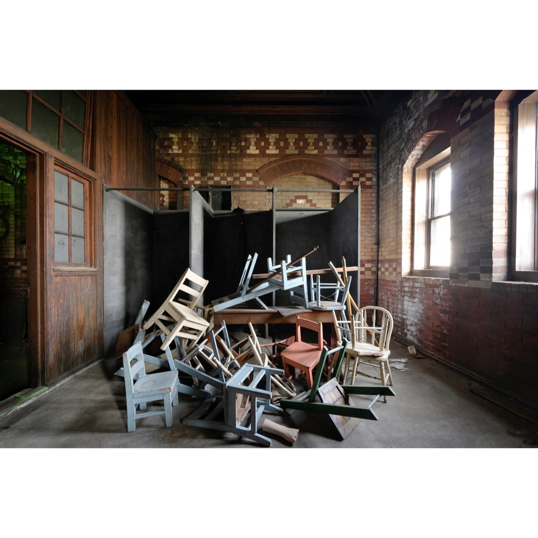 pile of wooden chairs in different colors in center of brick and tile room with natural light through the windows