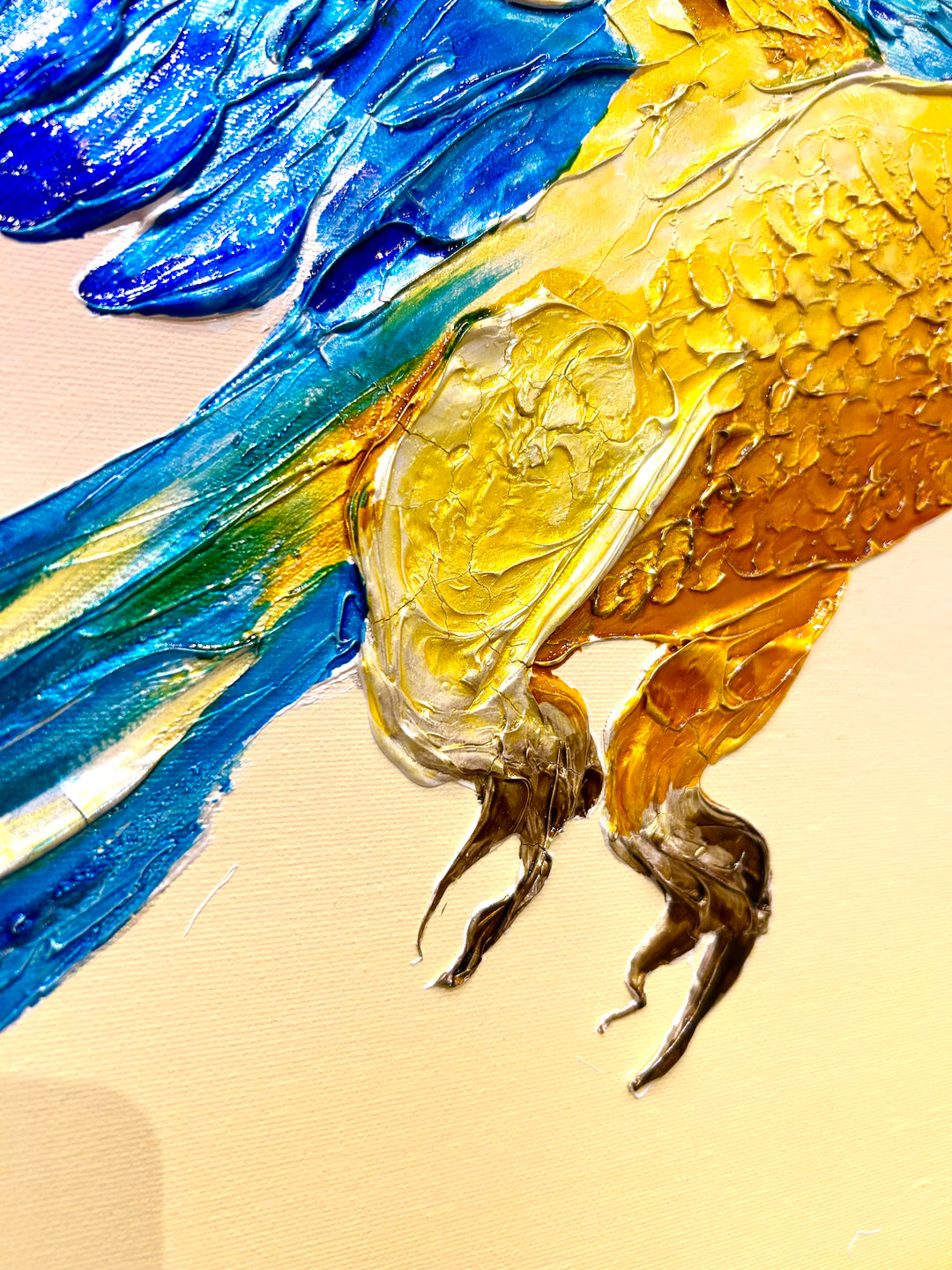 30” x 30” painting by French artist Moogly of a blue and yellow parrot in sunglasses with a pink and yellow ombre background. The parrot is depicted in mid-flight and made out of resin, giving it a textured and shiny finish.