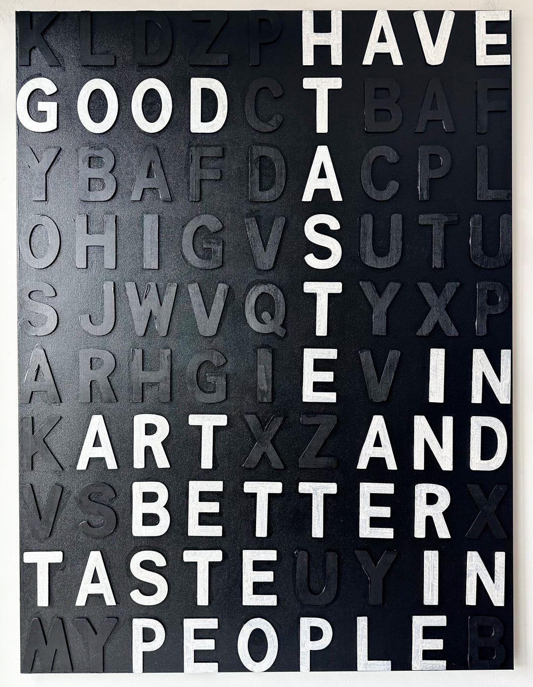 Steffanie Gerkin’s Have Good Taste Black 3D is a contemporary mixed-media typography artwork made with raised wood and acrylic letters on canvas, featuring a black monochrome alphabet grid with contrasting white letters that spell phrases including “Have Good Taste,” “Art,” “Better Taste,” and “People.”