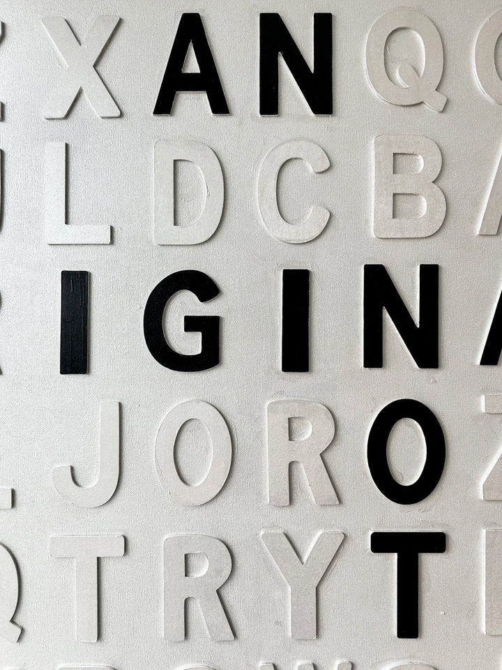 Contemporary 3D text artwork by Chicago artist Steffanie Gerkin titled I’m an Original 3D, featuring raised black and white wood letters arranged in a structured alphabet grid on a white canvas. The monochrome typographic composition spells the phrase “I’m an Original, Not a Print,” creating a bold conceptual wall art piece with graphic text-based design, pop art influence, and contemporary mixed-media style.