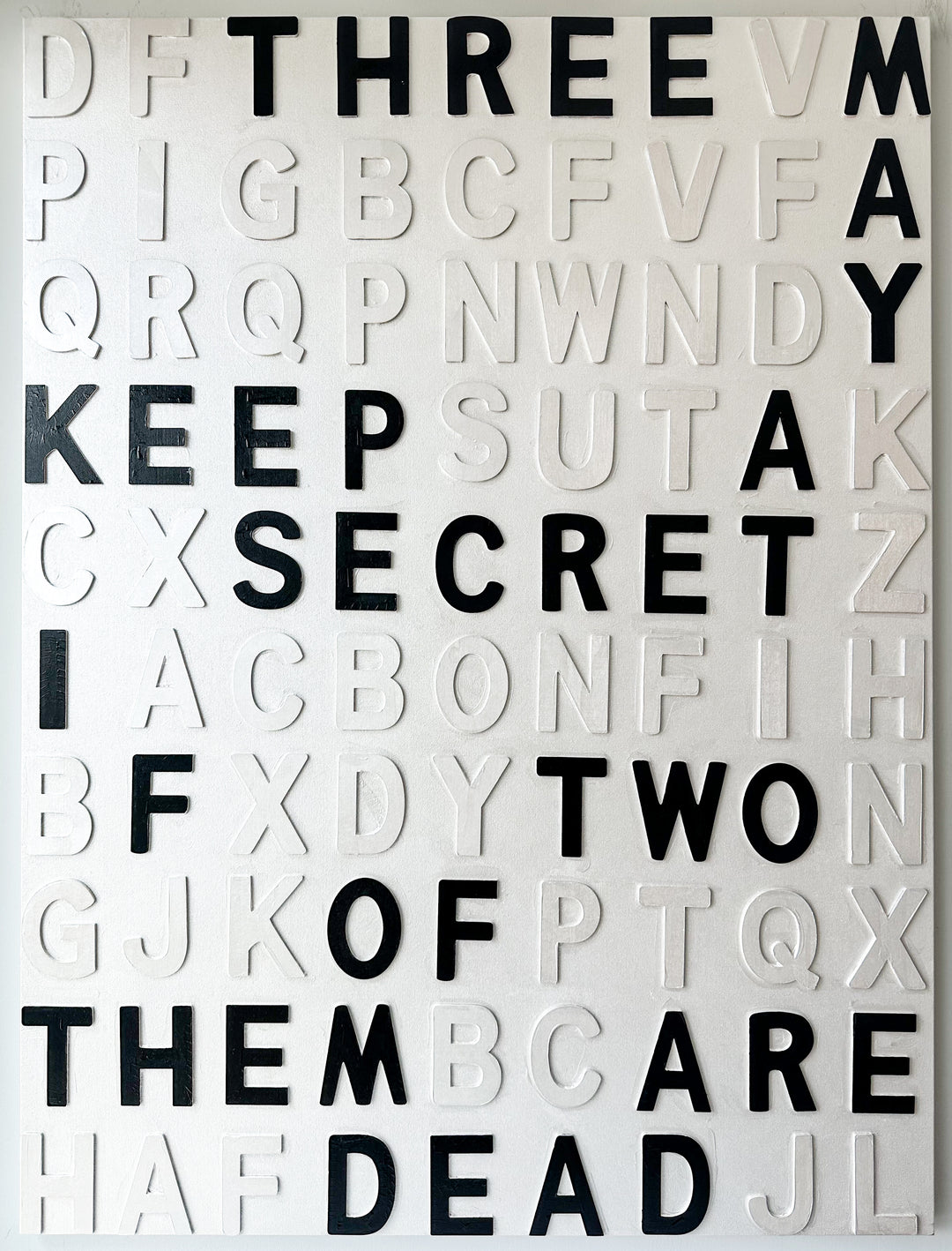 Contemporary 3D text artwork by Chicago artist Steffanie Gerkin titled Keep A Secret 3D, featuring raised black and white wood letters arranged in a structured alphabet grid on a white canvas. The typographic composition spells “Keep a Secret,” “Three May,” and “Two of Them Are Dead,” creating a bold monochrome mixed-media wall art piece with graphic, conceptual, and pop art qualities.