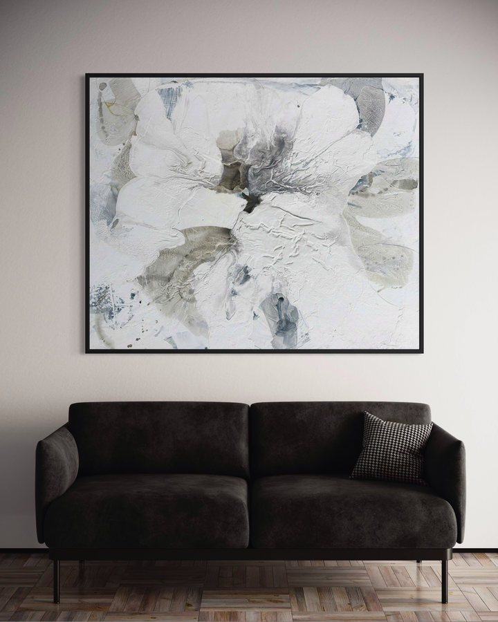Liz Barber, Poppy 6, acrylic paint, ink, and watercolor on canvas, 72 x 60 inches. Large abstract white flower form with textured layered petals in white, pale gray, and taupe around a dark charcoal center, with gray-blue accents, shown in a black frame above a dark charcoal sofa.