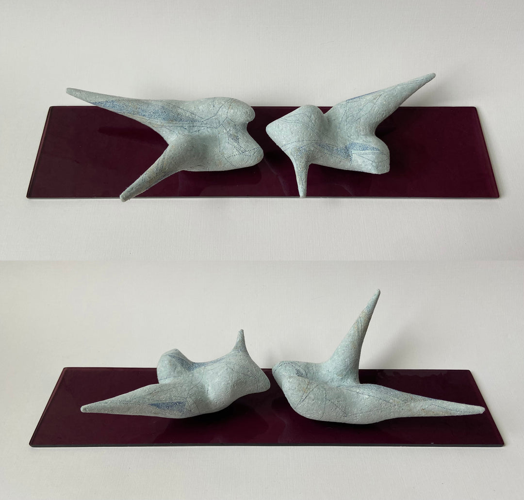 two abstract small shape blue bird like figurines sitting n glass shelf