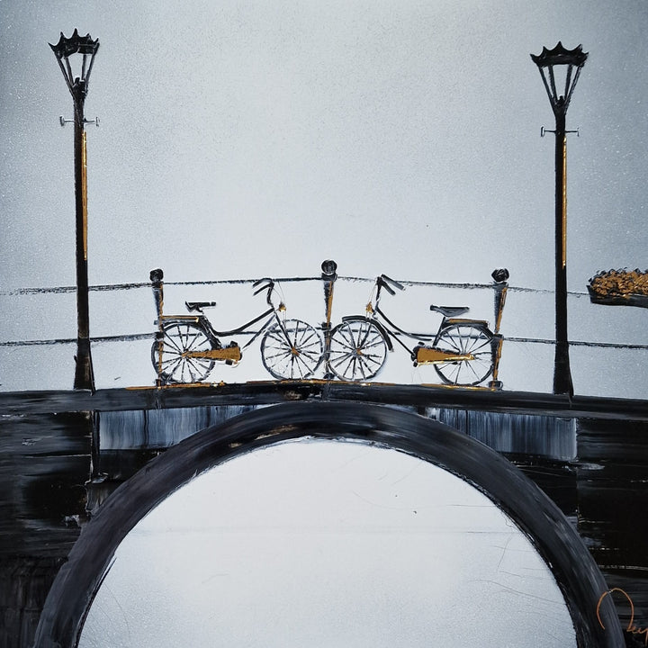 "Rendez-vous" by French artist Julien Rey — a mixed-media painting of two bicycles parked on a Parisian bridge, crafted with Chinese lacquer and gold leaf on canvas. Two classic city bikes with gold leaf accents rest against a bridge railing flanked by tall black street lamps, above a sweeping stone arch. A pale silver-gray sky fills the background, evoking quiet romance and urban poetry. Original contemporary French cityscape painting available at Morton Contemporary gallery.