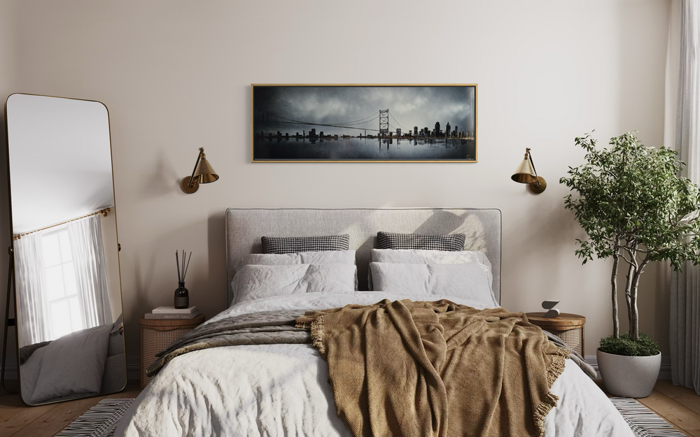 Julien Rey, Skyline, lacquer and gold leaf on board, 16 x 47 inches, shown framed above a bed in a bedroom with a tan throw blanket, a full-length mirror, and a potted plant.