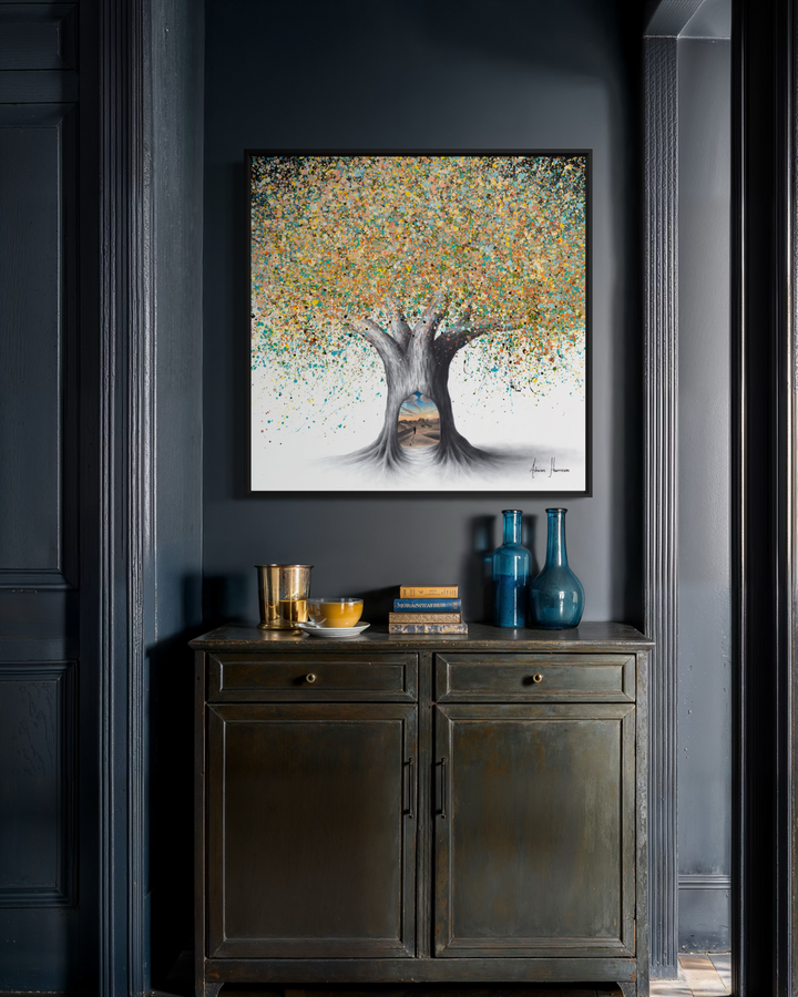 Ashvin Harrison, Tree of the Desert Oasis, coconut charcoal dust and acrylic on canvas, 36 x 36 inches, shown in a black frame hanging in a dark grey hallway above a dark green two-door cabinet holding books, a gold cup and two blue glass vases.