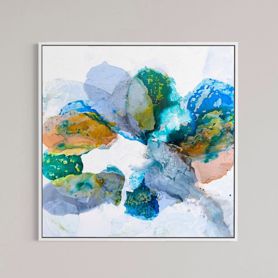 Liz Barber, Water's Edge 1, acrylic paint, ink, and watercolor on canvas, 48 x 48 inches. Abstract composition of overlapping rounded, stone-like shapes in teal, cobalt blue, lavender gray, ochre, and peach with speckled yellow-green texture on a white background, shown in a thin white frame on a light gray wall.