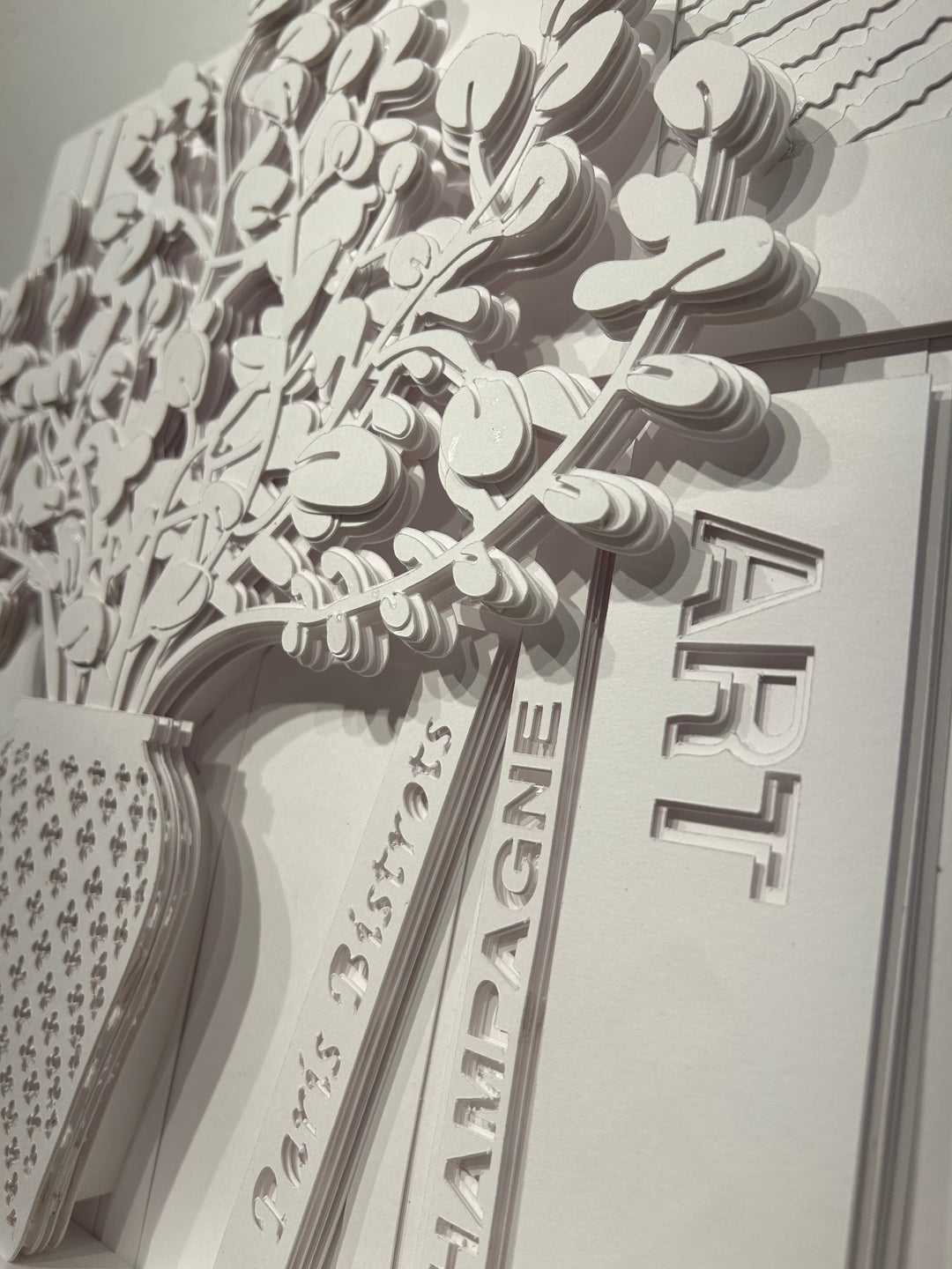 14"x14" layered white paper forming a vase with a fern over a wall.  